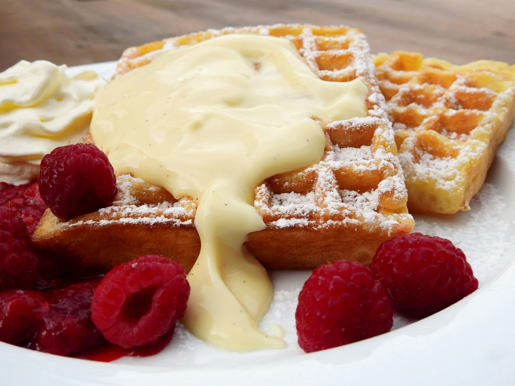 Close-up of waffles topped with cream and raspberries, perfect for breakfast.